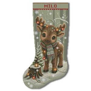 May include: A Christmas stocking in sage green featuring a brown reindeer wearing a patterned scarf and tangled in colorful string lights. The name MILO is printed in red at the top. The scene includes a tree stump, a lantern, and white snowflakes.
