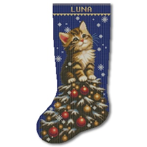 May include: A dark blue Christmas stocking featuring a brown tabby kitten sitting atop a snow-dusted evergreen tree decorated with red and gold ornaments. The name LUNA is printed in white letters at the top, surrounded by white snowflake patterns.