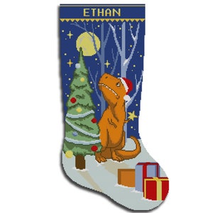 May include: A blue and white Christmas stocking with a dinosaur wearing a Santa hat standing next to a Christmas tree. The stocking has the name "ETHAN" embroidered on it.