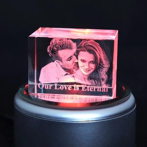 May include: A clear, rectangular crystal block featuring a laser-etched image of a couple, illuminated with a red glow. The text "Our Love is Eternal" is etched at the base. The crystal sits on a rotating base, creating a romantic effect.