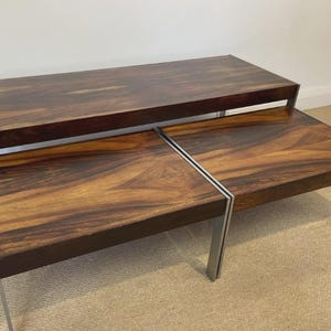May include: A set of three nesting tables featuring rectangular tops with a dark brown wood grain pattern and smooth surfaces. Each table is supported by four slender, straight metal legs with a silver finish, providing a stable structure.