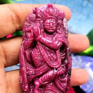 Puede incluir: Un colgante de rubí tallado que representa a una deidad hindú. El colgante es de color rosa intenso y tiene tallas intrincadas.