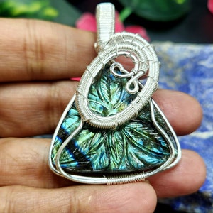 Può includere: Un ciondolo avvolto in filo d'argento con una pietra preziosa di labradorite intagliata con sfumature iridescenti verdi e blu. Il ciondolo ha la forma di una lacrima e presenta un delicato design in filo.