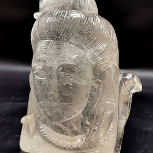 Könnte beinhalten: Eine transparente Kristallsculptur der hinduistischen Gottheit Shiva mit einer detaillierten Schnitzerei von Gesicht und Haaren. Die Skulptur ist etwa 15 cm hoch und aus klarem Quarz gefertigt.
