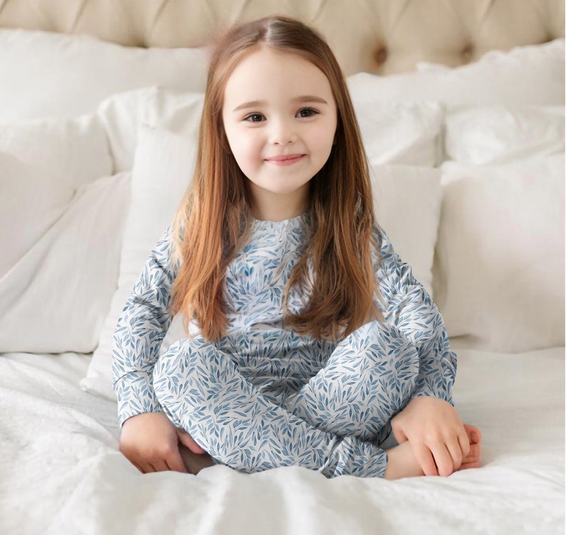 Op de afbeelding: Een jong kind draagt een blauwe en witte lange mouwen pyjama met een bladerenpatroon. De pyjama is gemaakt van zachte, comfortabele stof en is perfect om in te slapen of om in te relaxen in huis.
