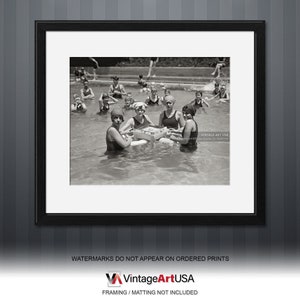 May include: Black and white photograph of a group of women in swimsuits playing a game in a swimming pool. The women are wearing swim caps and are sitting in the water, holding a game board.