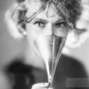 May include: A black and white photo of a person holding a silver cocktail glass in front of their face.