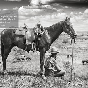 Puede incluir: Una fotograf&iacute;a en blanco y negro de un vaquero sentado en el suelo junto a un caballo. El vaquero lleva un sombrero y mira hacia el suelo. El caballo est&aacute; de pie con la cabeza gacha. Hay muchos otros caballos en el fondo, pastando en un campo.