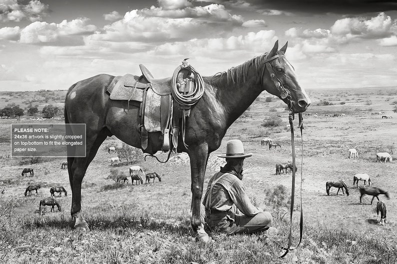 Puede incluir: Una fotograf&iacute;a en blanco y negro de un vaquero sentado en el suelo junto a un caballo. El vaquero lleva un sombrero y una camisa de manga larga. El caballo lleva una silla de montar y una brida. El fondo es un campo con otros caballos en la distancia.
