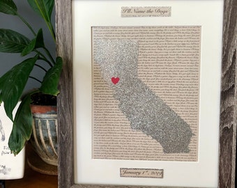 May include: Framed artwork featuring a map of California in silver glitter, with a red heart marking a location. The text "I'll Name the Dogs" is at the top, and "January 1st, 2019" is at the bottom. The frame is a rustic gray wood.