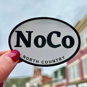 May include: White oval sticker with black text that reads "NoCo NORTH COUNTRY".