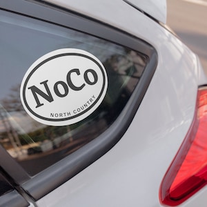 May include: White oval sticker with the text "NoCo North Country" on a white car.