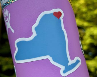 May include: A blue outline of the state of New York with a red heart over the city of New York. The sticker is on a purple background.