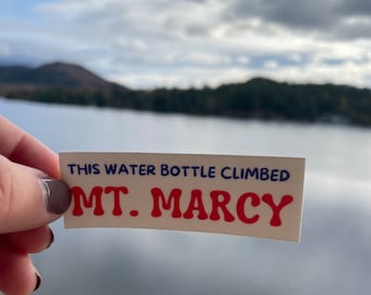 May include: A white sticker with blue and red text that reads "This water bottle climbed Mt. Marcy".