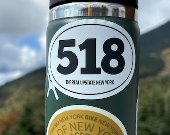 May include: A green insulated water bottle with a white oval sticker that says "518 THE REAL UPSTATE NEW YORK". There is a smaller yellow sticker on the bottle that says "ORK SKI NEW YORK BIKE NEW YORK OF NEW YO".