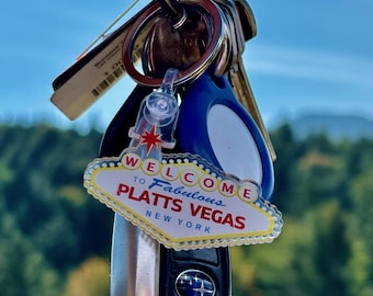 May include: A collection of keys on a key ring, including a car key and a keychain with a "Welcome to Fabulous Platts Vegas New York" design. The keychain has a red star and a white and yellow border.