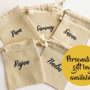 May include: Five beige burlap gift bags with drawstring closures, each personalized with a name in black script: Pam, Sammy, Susan, Rajaa, and Nadia. A yellow circle states "Personalized gift bag available."