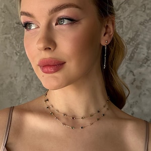 May include: A double-strand gold chain necklace featuring small, multi-colored gemstone beads spaced evenly along the delicate links, paired with a single matching drop earring consisting of a thin gold chain and small beads.