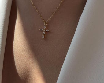 May include: A gold-colored necklace with a cross pendant. The cross is adorned with small, clear gemstones. The necklace is displayed against a white garment and skin.