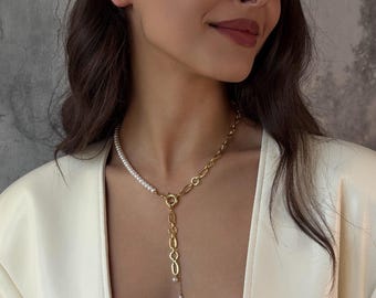 May include: A gold-toned metal chain necklace featuring a section of small white pearls on one side and a toggle clasp closure at the center. A vertical drop chain hangs from the clasp, accented with a single small pearl at the very bottom end.