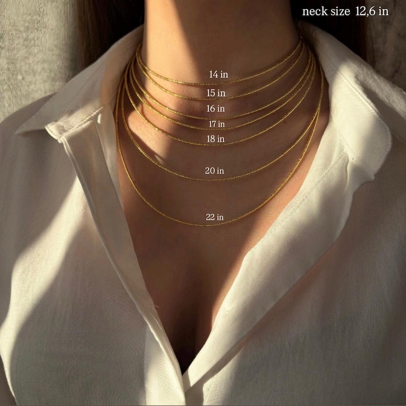 a close-up view of a person's neck and chest area, with a series of gold necklaces of varying lengths and sizes. The necklaces are arranged in a descending order from 14 in. to 22 in.