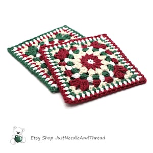 May include: Two square crochet coasters in a granny square pattern. The coasters feature a red, green, and cream color scheme. The edges are finished with a dark green border. The Etsy shop name "JustNeedleAndThread" is visible in the bottom left corner.