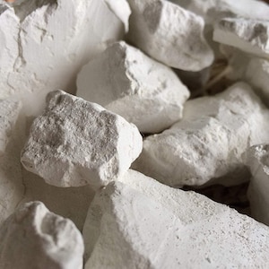 Könnte beinhalten: Eine Ansammlung von unregelmäßigen, mattweißen Kreidegesteinen mit rauen, gezackten Kanten und einer porösen, pudrigen Textur. Die Steine variieren in Größe und Form und weisen natürliche Brüche sowie unebene Oberflächen im gesamten Gesteinshaufen auf.