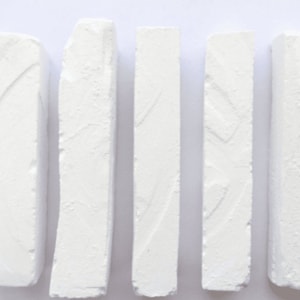 May include: Five white chalk sticks arranged horizontally on a white surface.