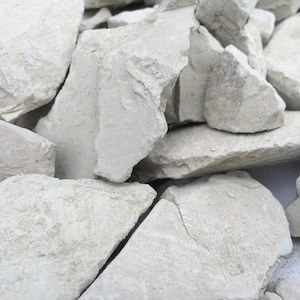 May include: A collection of irregular, jagged chunks of off-white chalky rock. The pieces vary in size and shape, featuring rough, matte surfaces with visible cracks, sharp edges, and a powdery, light-coloured texture throughout the entire cluster.