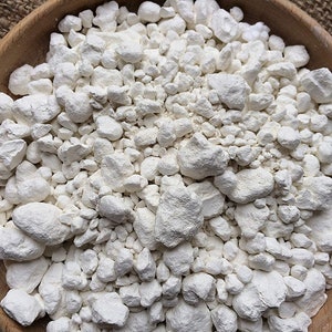 May include: A close-up view of a bowl filled with white, irregularly shaped, chalky-looking mineral rocks.