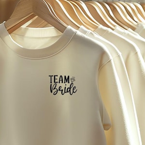 Peut inclure: Un groupe de sweat-shirts à col rond blanc cassé avec le texte "TEAM Bride" imprimé sur le devant du premier sweat-shirt.
