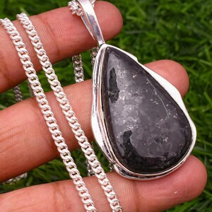 May include: A silver chain necklace with a black teardrop-shaped pendant. The pendant is made of a dark, sparkly stone.