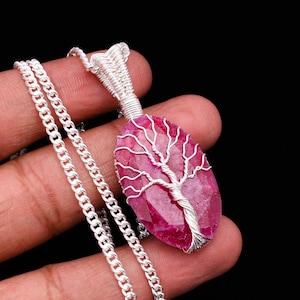 Pode incluir: Um colar de corrente de prata com um pingente de pedra preciosa rosa com um design de árvore envolto em arame.