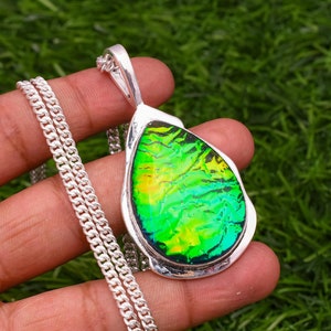 Può includere: Una collana con catena d'argento con un ciondolo a forma di lacrima con una pietra iridescente verde e gialla.