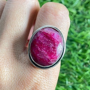 May include: A silver ring with a large, oval-shaped, deep pink ruby gemstone.