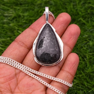 May include: A silver chain necklace with a teardrop-shaped pendant featuring a black gemstone with silver flecks.