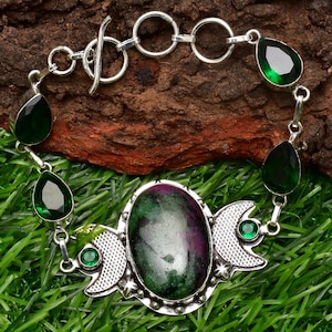 May include: A silver bracelet featuring a green gemstone and a crescent moon design. The bracelet has a toggle clasp.