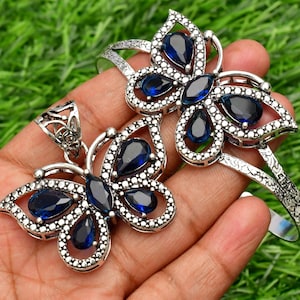 May include: A silver butterfly pendant and bracelet set with blue gemstone accents. The jewelry is made of silver and features a detailed butterfly design with blue gemstones.