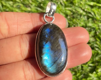 Puede incluir: Un colgante de plata con una gran piedra ovalada de labradorita con reflejos azules y verdes iridiscentes.