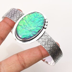 Pode incluir: Um bracelete de punho de prata com uma grande gema oval verde iridescente engastada no centro. O bracelete tem um design texturizado.