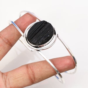 May include: Silver bangle bracelet with a black tourmaline gemstone. The bracelet is open and adjustable.
