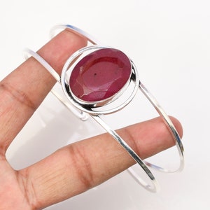 Puede incluir: Un brazalete de plata con una piedra preciosa roja engastada en un diseño circular.
