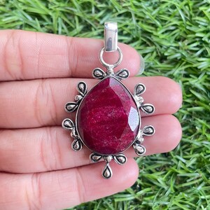 Pode incluir: Um pingente de prata com uma grande gema vermelha escura em forma de lágrima engastada em uma moldura de prata decorativa.