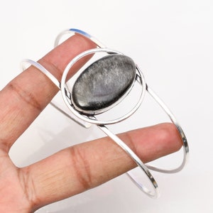 Op de afbeelding: Zilveren armband met een grote ovale zwarte edelsteen in een cirkelvormig ontwerp.