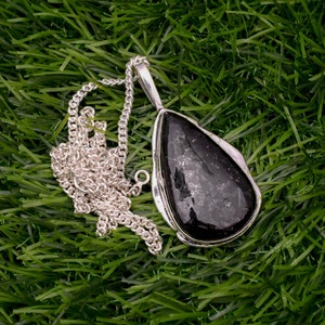 May include: A silver chain necklace with a teardrop-shaped pendant featuring a black gemstone. The pendant has a silver setting and the gemstone has a sparkly, speckled texture.
