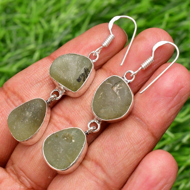 May include: A pair of silver dangle earrings with two green gemstone drops on each earring.