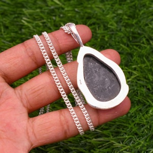 May include: A silver chain necklace with a teardrop-shaped pendant featuring a black stone. The pendant has a detailed silver border.