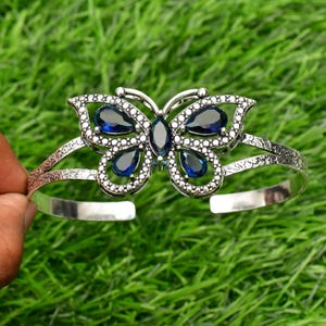 May include: Silver butterfly bracelet with blue gemstone accents. The bracelet is open and adjustable.
