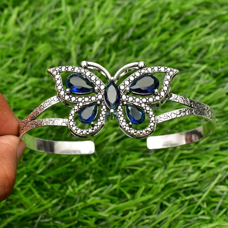 May include: Silver butterfly bracelet with blue gemstone accents. The bracelet is open and adjustable.
