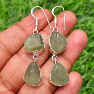 May include: A pair of silver dangle earrings with two green gemstone drops. The gemstones are irregularly shaped and have a translucent, slightly cloudy appearance.
